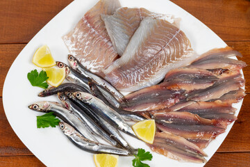 Raw mixed fish on a white plate. Fillets of saithe and anchovies. Flat lay. Closeup.