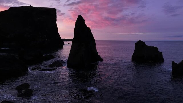 Aerial view of dark, jagged Valahnukur cliffs meeting the tranquil sea under a vibrant pink and purple sunset sky, Keflavik, Reykjanesbaer, Iceland.