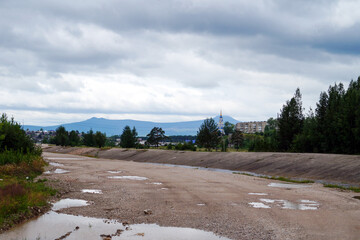 Dry urban riverbed with puddles and village skyline after rain