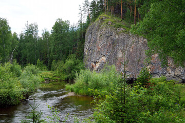 Rocky cliff above forest river with summer greenery around