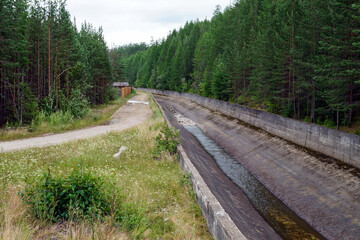 Narrow concrete canal with stream near forest and rural path