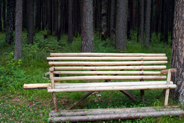 Rustic wooden bench in forest made from raw logs and branches