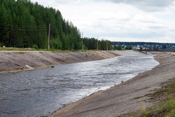 Full river flowing through concrete channel near forest and village