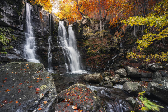 View of cascading waterfalls plunge amidst a symphony of autumn colors, with leaves scattered on rocks in Lizzano In Belvedere, Emilia-Romagna, Italy.