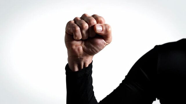 A strong arm clad in black rises to hold a tightly clenched fist steady against a bright white backdrop. The slow and deliberate motion conveys an unwavering commitment to a cause.