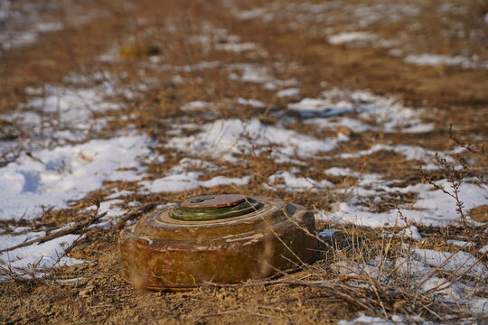 An anti-personnel mine is lying on the ground among the soil and snow.