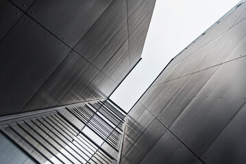 Abstrakcyjne ujęcie z dołu nowoczesnej metalowej elewacji budynku na tle jasnego nieba © ErOn