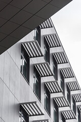 Nowoczesna szara fasada budynku z powtarzalnym wzorem okien i przemysłowymi osłonami przeciwsłonecznymi © ErOn