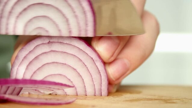 Close up of female chopping red onion on wooden cutting board with a knife