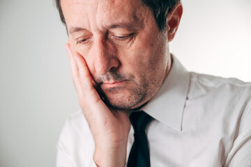 Obraz premium Businessman in white shirt and dark tie, eyes gently closed and head resting heavily on his hand in profound fatigue.