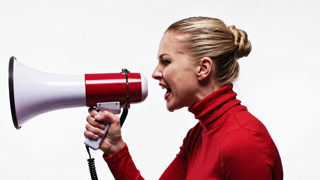 A determined blonde woman in a vibrant red turtleneck passionately shouts into a red and white megaphone, amplifying her voice for social change. The clean white background emphasizes her message with
