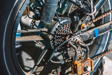 Obraz premium Bicycle drivetrain on an urban street, showing chain, cassette, and rear derailleur in gritty detail. Industrial textures and wear highlight cycling, mechanics, and everyday transport
