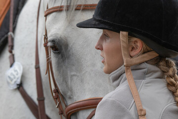 das Gesicht einer jungen Springreiterin im Profil vor dem Kopf ihres vertrauensvollen Pferdes © mavcon