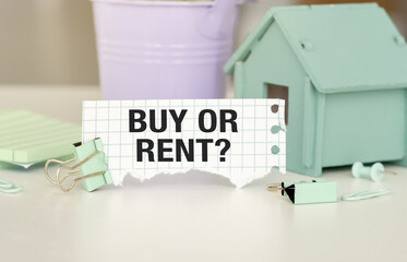 Buy Or Rent text on a scrap of paper against the background of a wooden figurine of a house on the table