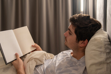 Young man reading book in bed before sleep