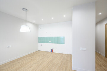 A minimalist room with light wooden flooring, white walls, recessed ceiling lights, a pendant lamp, and a turquoise tile accent wall &mdash; clean, bright, modern space.