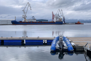 inflatable motorboat on a pier against the backdrop of a cargo ship in a seaport