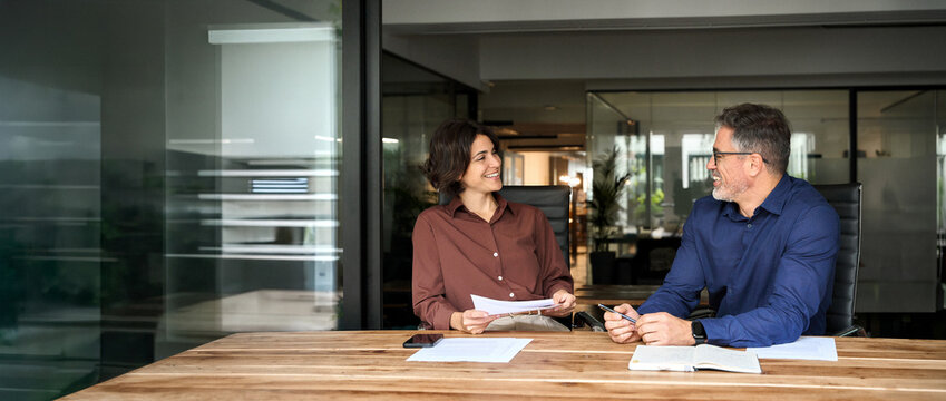 Happy professional executives team discussing papers working together in office. Female attorney manager consulting client during legal advice corporate meeting. Two colleagues communicating at work.
