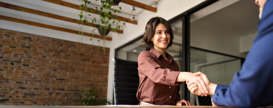 Happy young business woman bank manager handshaking client at meeting. Smiling female hr hiring recruit at job interview, insurance agent, lawyer making contract deal at work with business handshake.