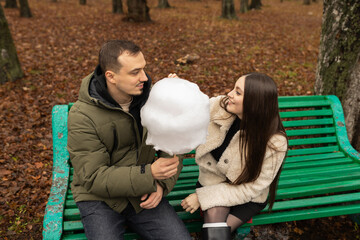 Young couple eating cotton candy on park bench 