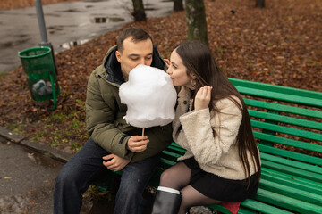 Young couple eating cotton candy on park bench 