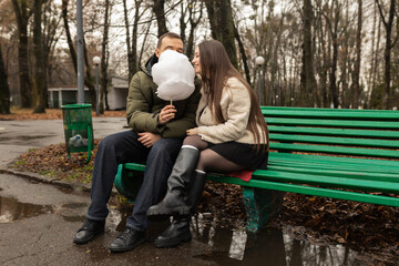 Young couple eating cotton candy on park bench 