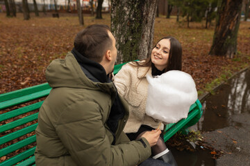 Young couple eating cotton candy on park bench 