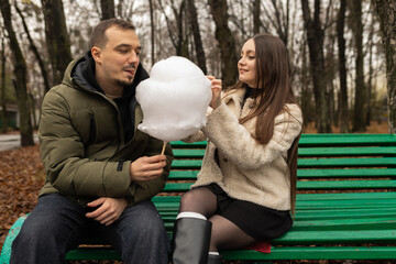 Young couple eating cotton candy on park bench 