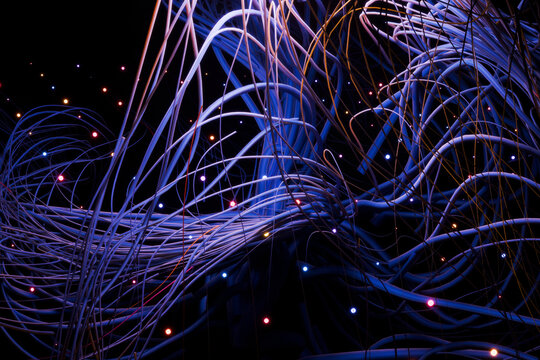 Chaotic yet beautiful 3D render of data streams. Glowing points of light represent information packets moving through a complex web of interconnected fiber lines