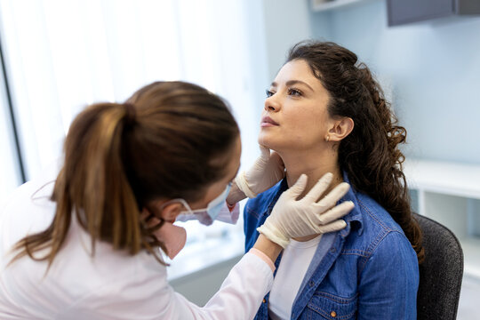 Female doctor performing thyroid or neck examination on patient. Professional healthcare provider conducting physical diagnostic checkup and lymph node screening in modern medical clinic.