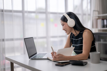 Young asian woman working from home attending online meeting taking notes