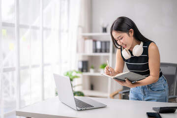 Young asian businesswoman taking notes in notebook while working at office