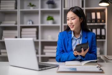 Asian businesswoman using calculator and working with laptop in office