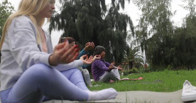 Diverse ethnic women doing yoga meditation class outdoor - Multi generational group, diversity and healthy lifestyle concept