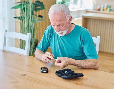 Portrait of senior man using lancet on finger for checking blood sugar level with glucose meter. Healthcare and medical, diabetes, glycemia concept