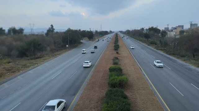 A beautiful winding road going through a patch of green trees on each side.Kashmir Road near Chattar Park, Punjab, Pakistan (01-23-2026) car and trafice View of Ring Road, Ring Road interexchange Isla