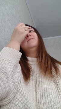 Woman applying eye drops while sitting indoors. Close-up selfie-style handheld video, natural lighting, daily healthcare routine.