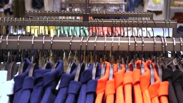 Diverse assortment of vibrant men's apparel, including polo shirts and sweaters, hanging on display racks in a retail store, showcasing the latest fashion trends and seasonal collections