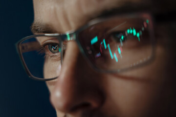Close-up of a focused trader wearing glasses with a glowing stock market chart reflection. Serious...