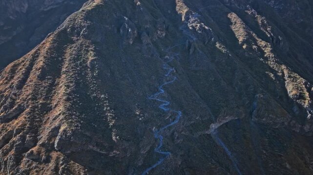 Drone approaches the trail down to the oasis as the ridgeline keeps the path in shadow, while morning light floods the rest of Colca Canyon, creating dramatic contrast and depth.