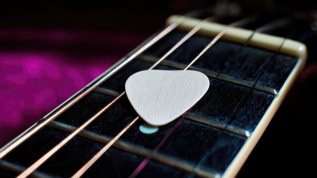 Close-up of a white guitar pick resting on the strings of a fretboard. Concept Close-Up Guitar Detail, White Pick on Strings, Fretboard Texture, Musical Gear Photography, Stringed Instrument Focus