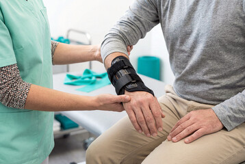 Fototapeta premium Professional physiotherapist examining patient wearing wrist brace in rehabilitation clinic
