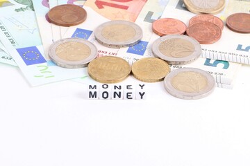 Close-up of a pile of euro banknotes and euro coins with small white cubes with letters in front of them spelling out "money"