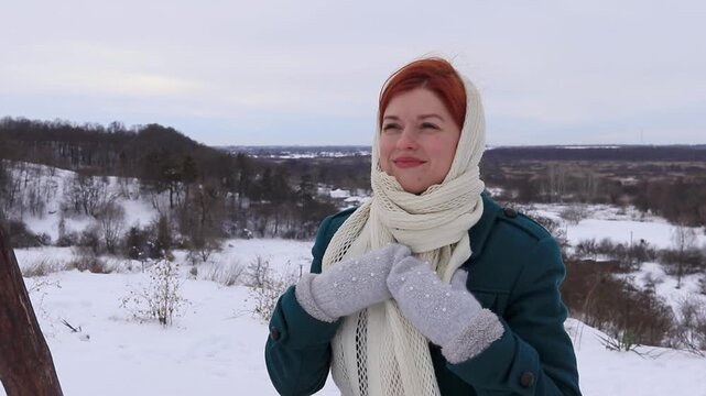 Beautiful girl with red hair in a warm coat and knitted scarf against a snowy landscape. Winter portrait, calm mood, natural light and a sense of comfort.