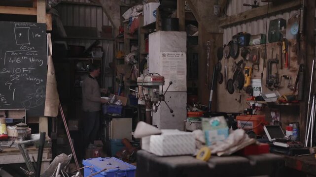 A workshop is filled with tools and materials as people work late into the night on different projects. Focus is on hands moving, crafting, and building in dim light.