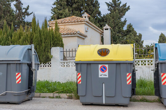 Color-coded waste and recycling bins in Spain help residents sort household waste. Yellow lids are for plastics and cans, green for glass, and grey bins for general non-recyclable waste.