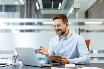 Obraz premium Businessman actively participating in a video call on his laptop from a modern office, taking notes and discussing ideas during an online virtual meeting