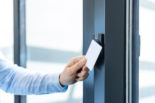 Hand holding white access card to an rfid reader, unlocking an electronic office door for secure, contactless entry and employee identification in a modern corporate building