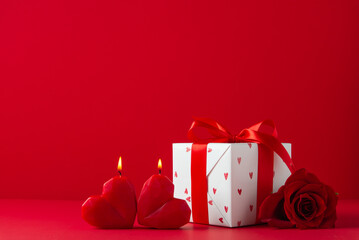 Gift, present box decorated with red ribbon and hearts, red rose flowers, heart shaped candles on red background. Valentine's day, February 14, birthday, 8 march women's day gift. Love and romance.
