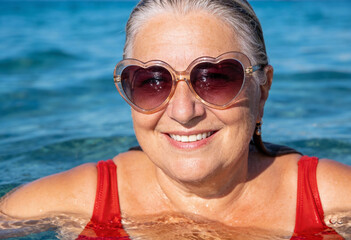 &auml;ltere Frau beim Schwimmen im Meer mit herzf&ouml;rmiger Sonnenbrille